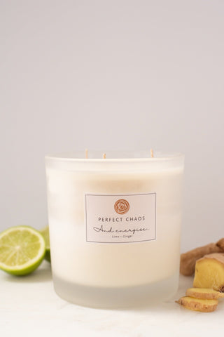 A frosted glass candle jar with three wicks labeled perfect chaos scented with lime and ginger with long hours burn time