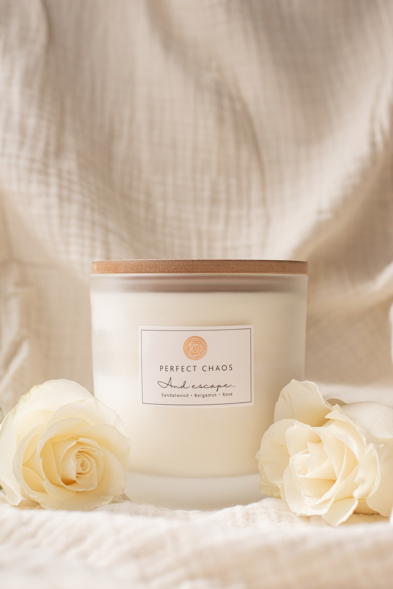 A creamy white scented frosted glass candle with wooden lid perfect chaos and escape sandalwood bergamot soap notes hours burn time
