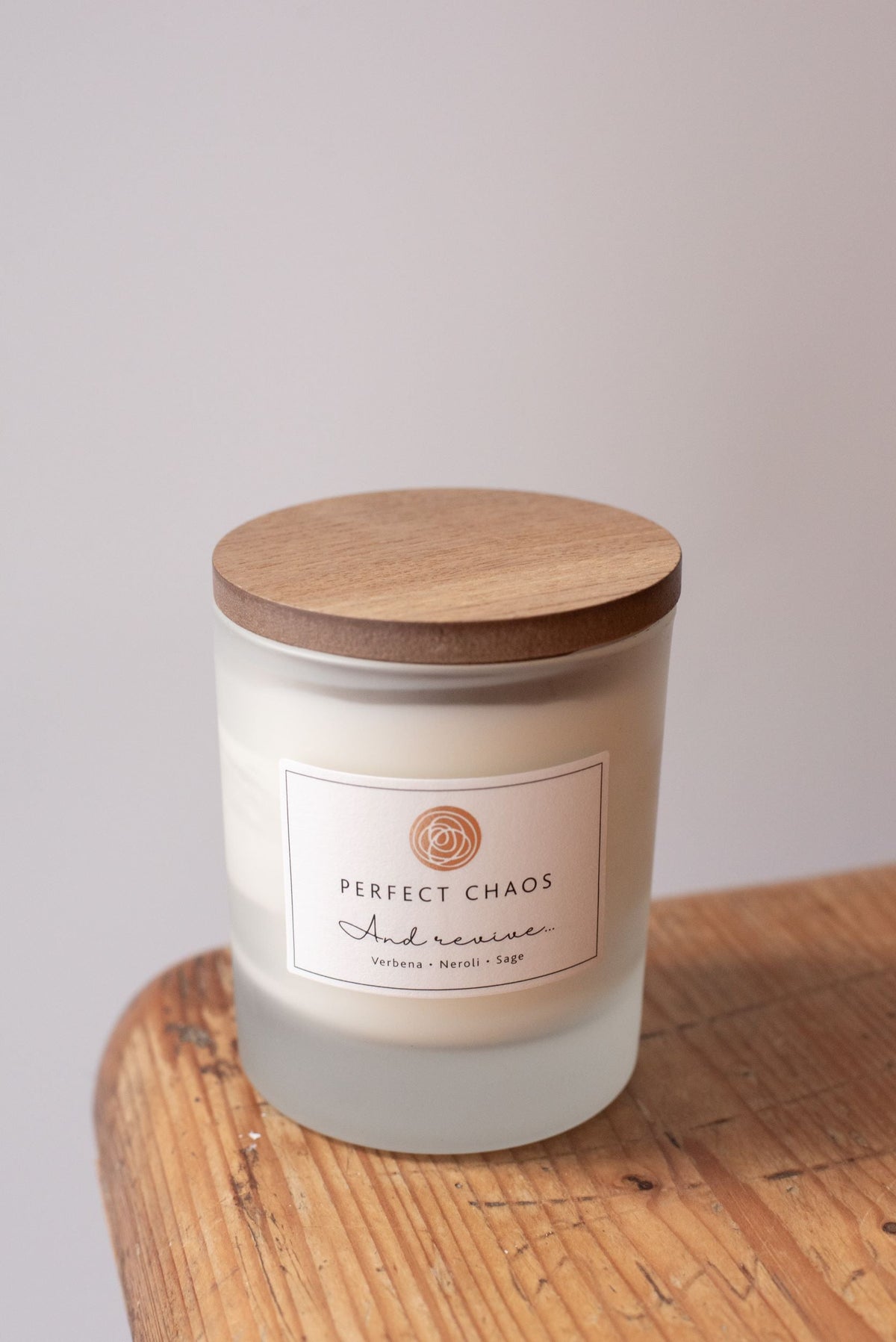 A frosted glass candle jar with natural wood lid and perfect chaos label offers long hours burn time