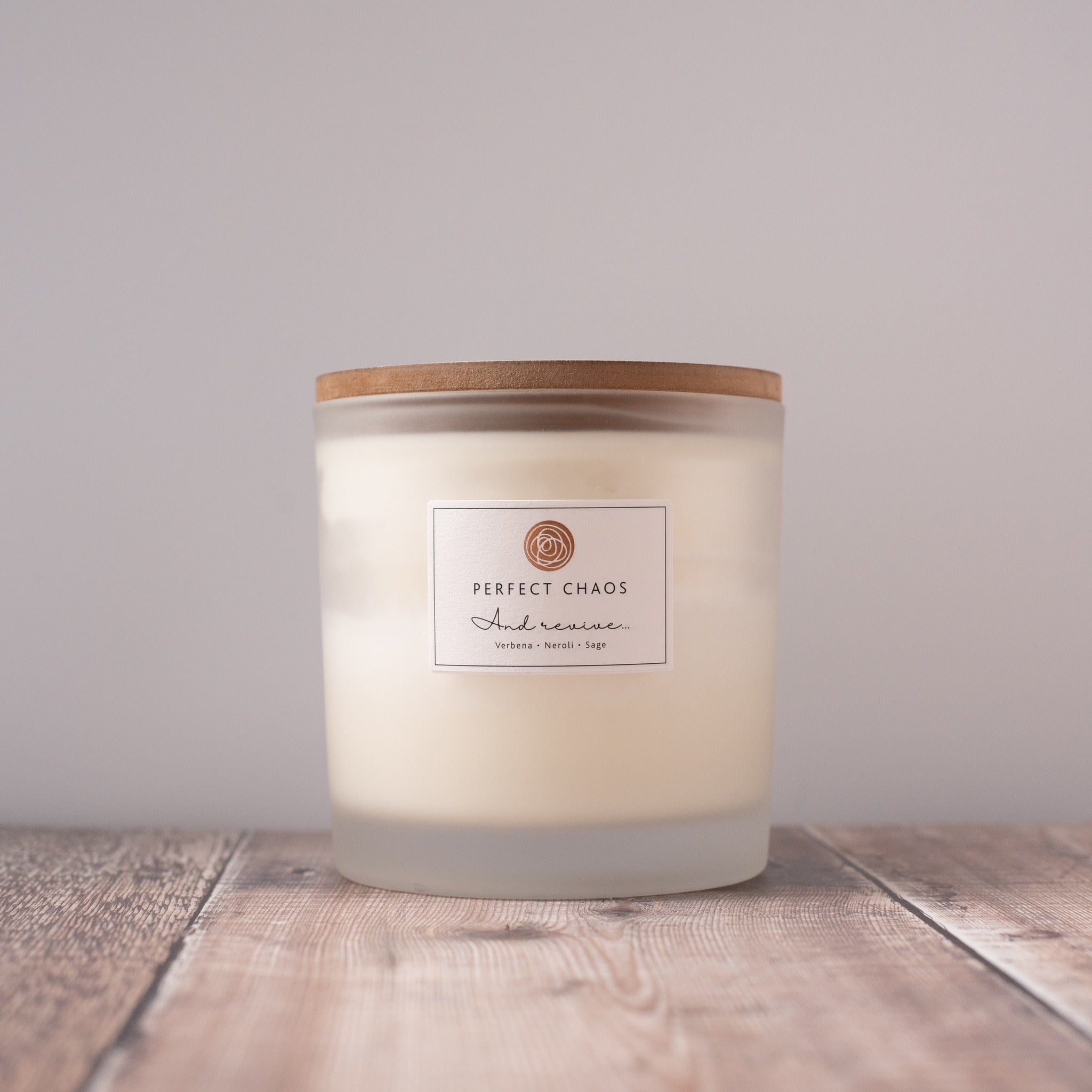A frosted glass candle jar with wooden lid by perfect chaos and revive with verbena neroli sage and hours burn time