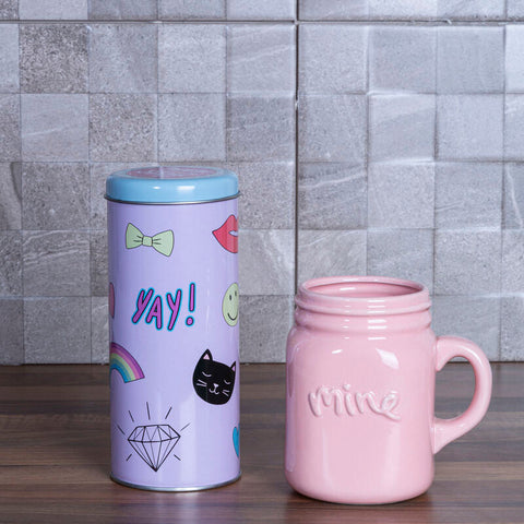 Pastel purple cylindrical fun times storage canister with light blue lid and colorful cartoon decals next to pink mug