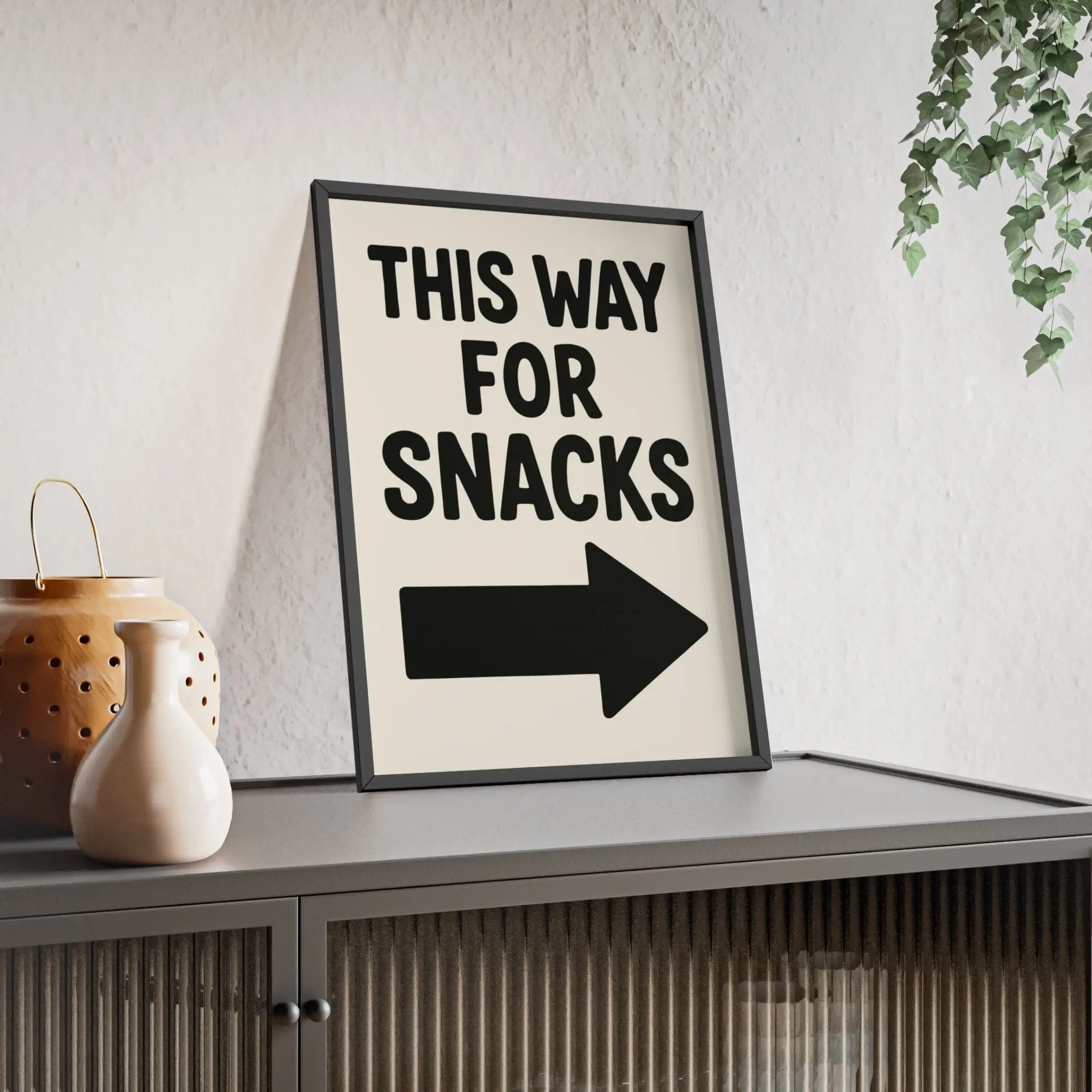 Black-framed funny kitchen poster with bold black this way for snacks text and arrow on off-white background