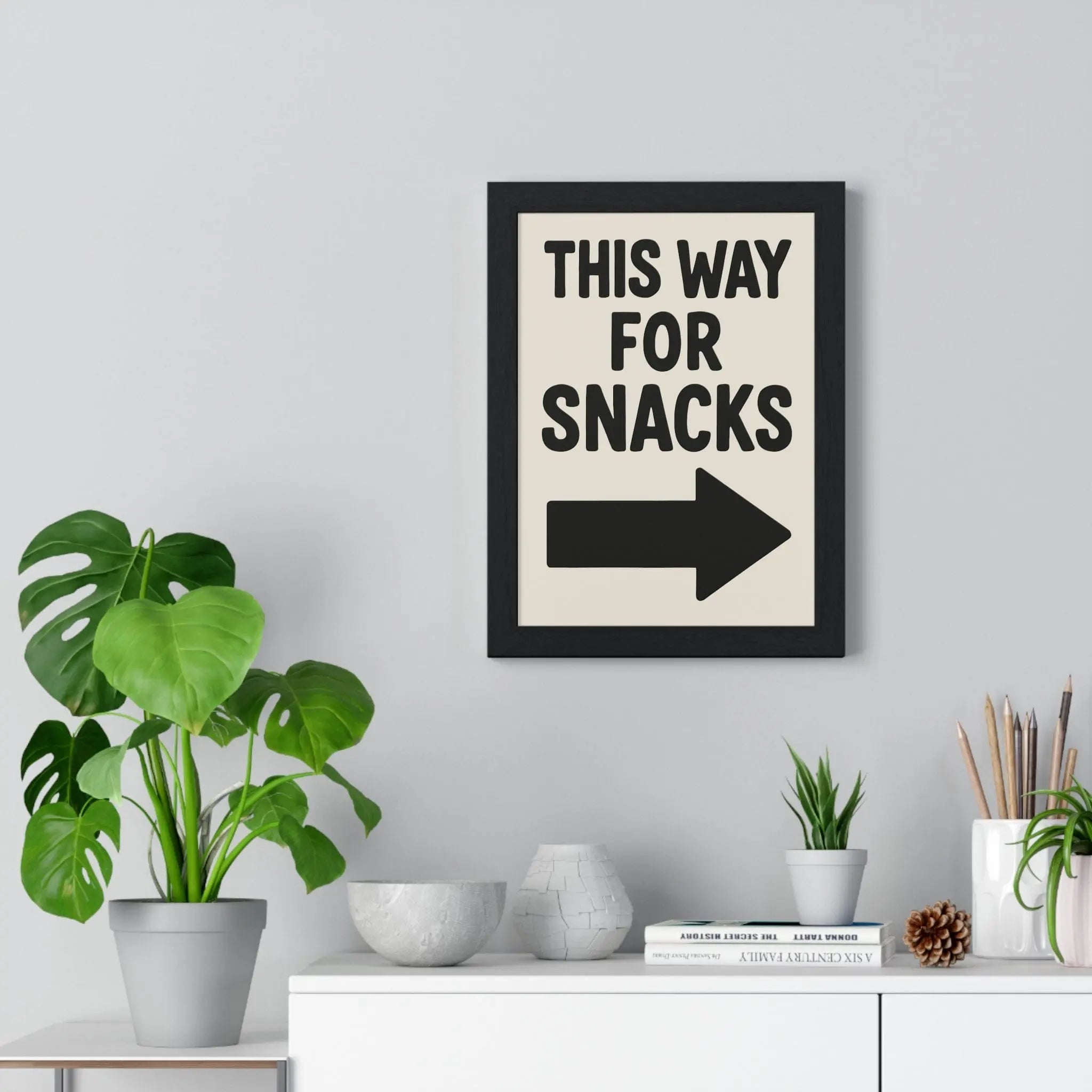 Black-framed funny kitchen poster with cream background and bold black text this way for snacks and arrow print