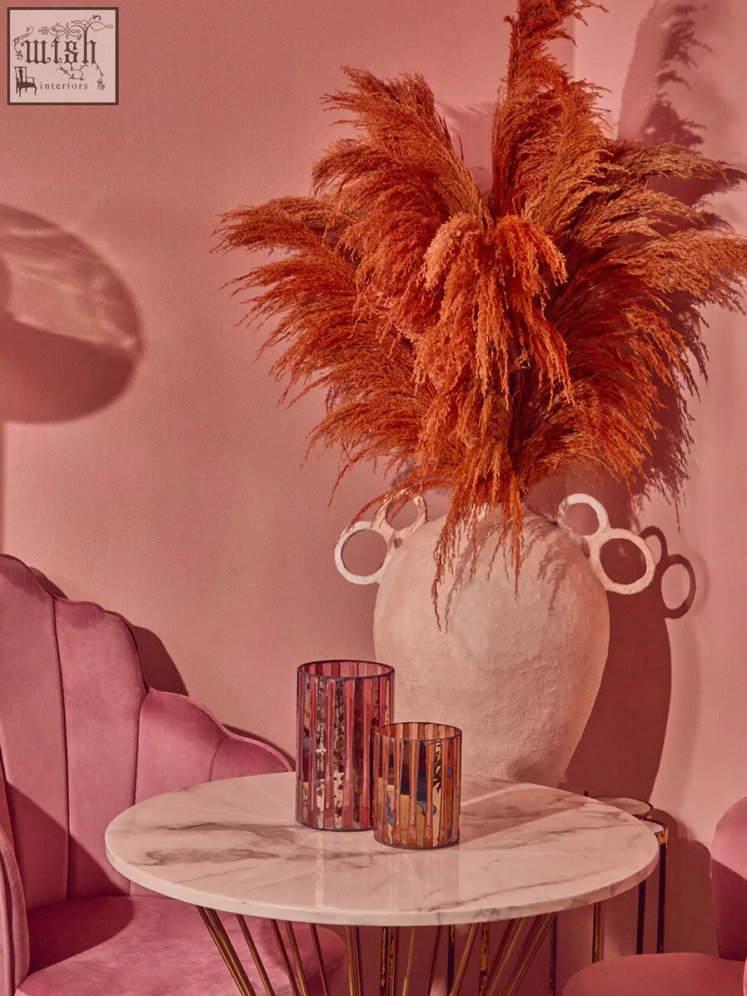 A tall white textured large candle holder with ringed handle design holding orange pampas grass for gaia pink decor