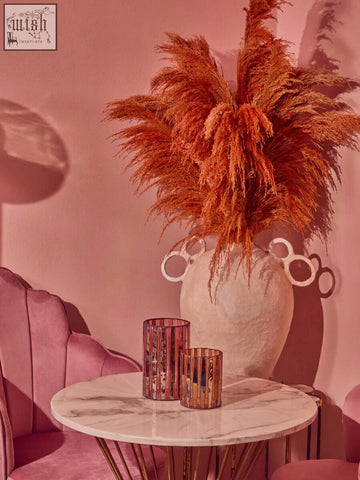 A tall white textured large candle holder with ringed handle design holding orange pampas grass for gaia pink decor