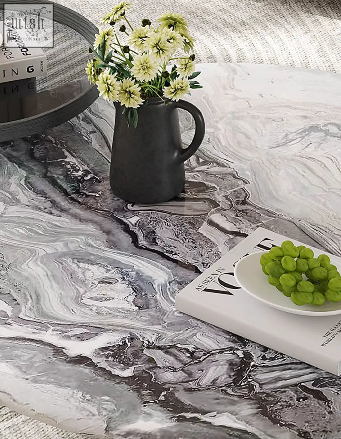 A matte black ceramic pitcher with pale green flowers on a galatea round nesting marble coffee table with marble top