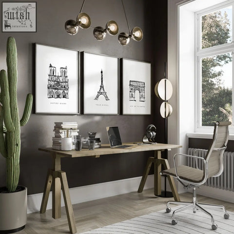 Three framed black-and-white line art paris landmarks wall art prints hang on dark gray wall above wooden desk