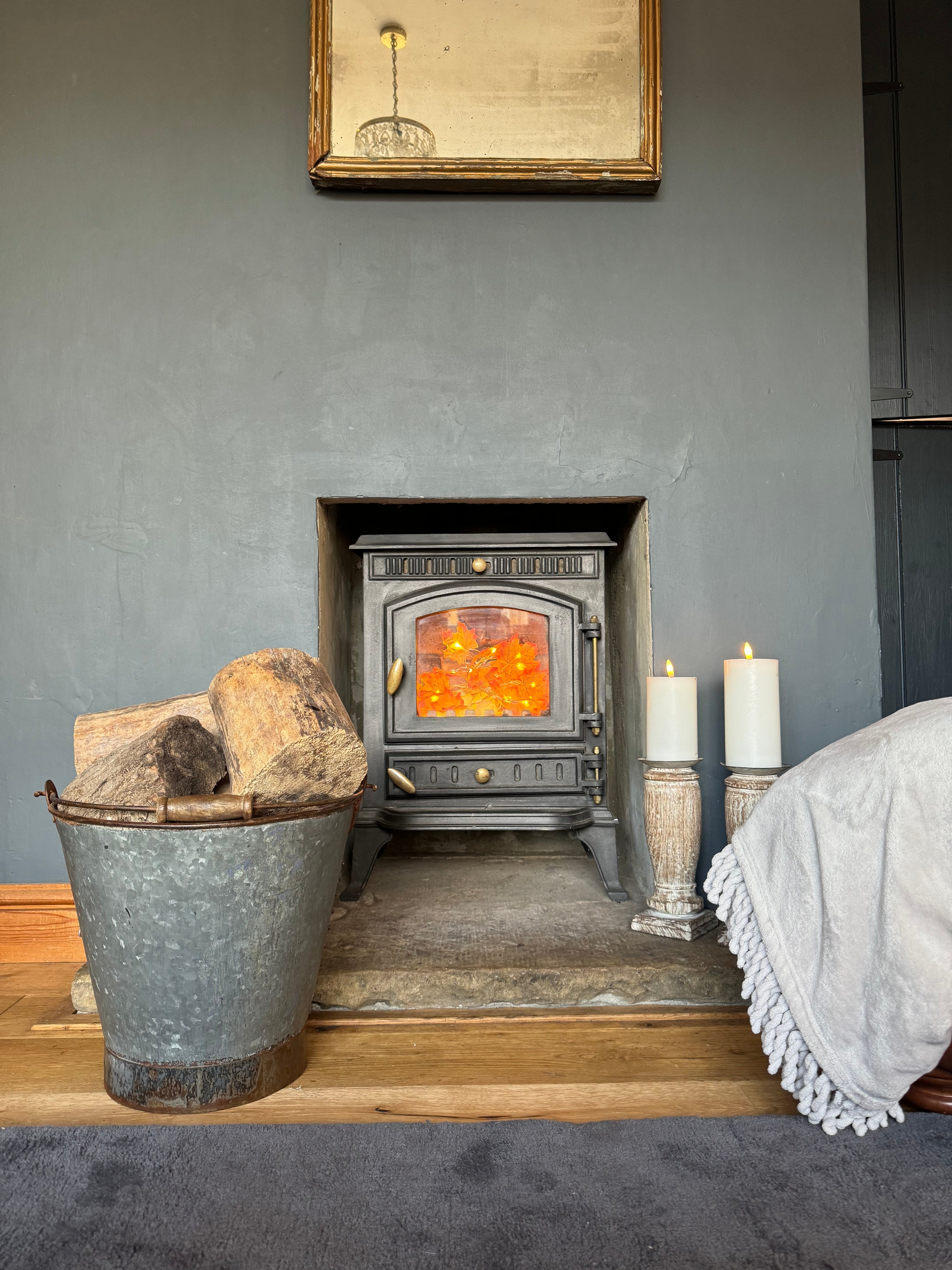 Black cast iron wood-burning stove with glowing fire next to galvanised log basket perfect for christmas tree or plants