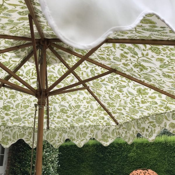A cream garden umbrella with scalloped edges and a hand block printed canopy featuring green botanical patterns