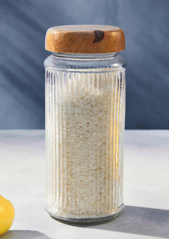 Clear glass storage jar with vertical ridges filled with white rice and a natural mango wood lid