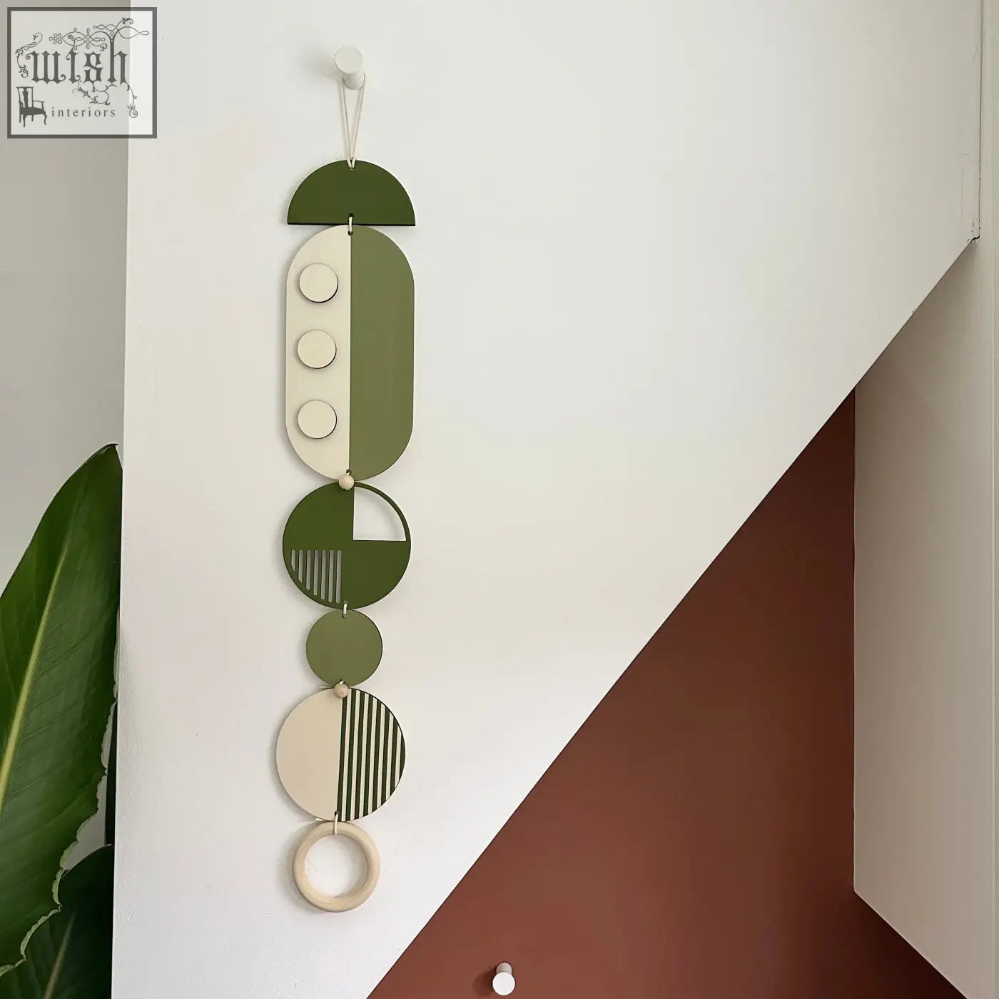 A modern wall art piece featuring layered olive green and cream wooden shapes with minimalist geometric patterns