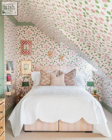 A cozy bedroom with a bed featuring a white quilted coverlet and pink-striped base against mediterranean charm geraniums wallpaper