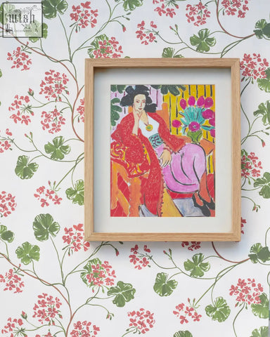 A framed artwork with a stylized portrait of two women in red and pink on bold yellow stripes, perfect for mediterranean charm and geraniums wallpaper decor