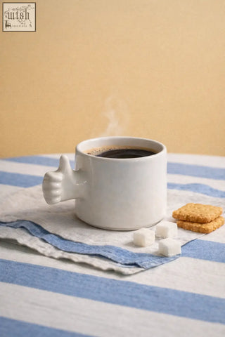 White ceramic mug with thumb-shaped handle filled with steaming black coffee from 4am product design cups series