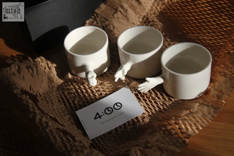 Three white ceramic mugs with sculpted hand-like handles handmade porcelain coffee cups by 4am product design