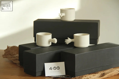 White ceramic gesture cups with sculpted hand handles on black boxes handmade porcelain 4am product design