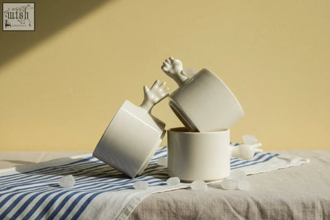 White ceramic handmade porcelain coffee cups with sculpted hand handles stacked on striped cloth by 4am product design