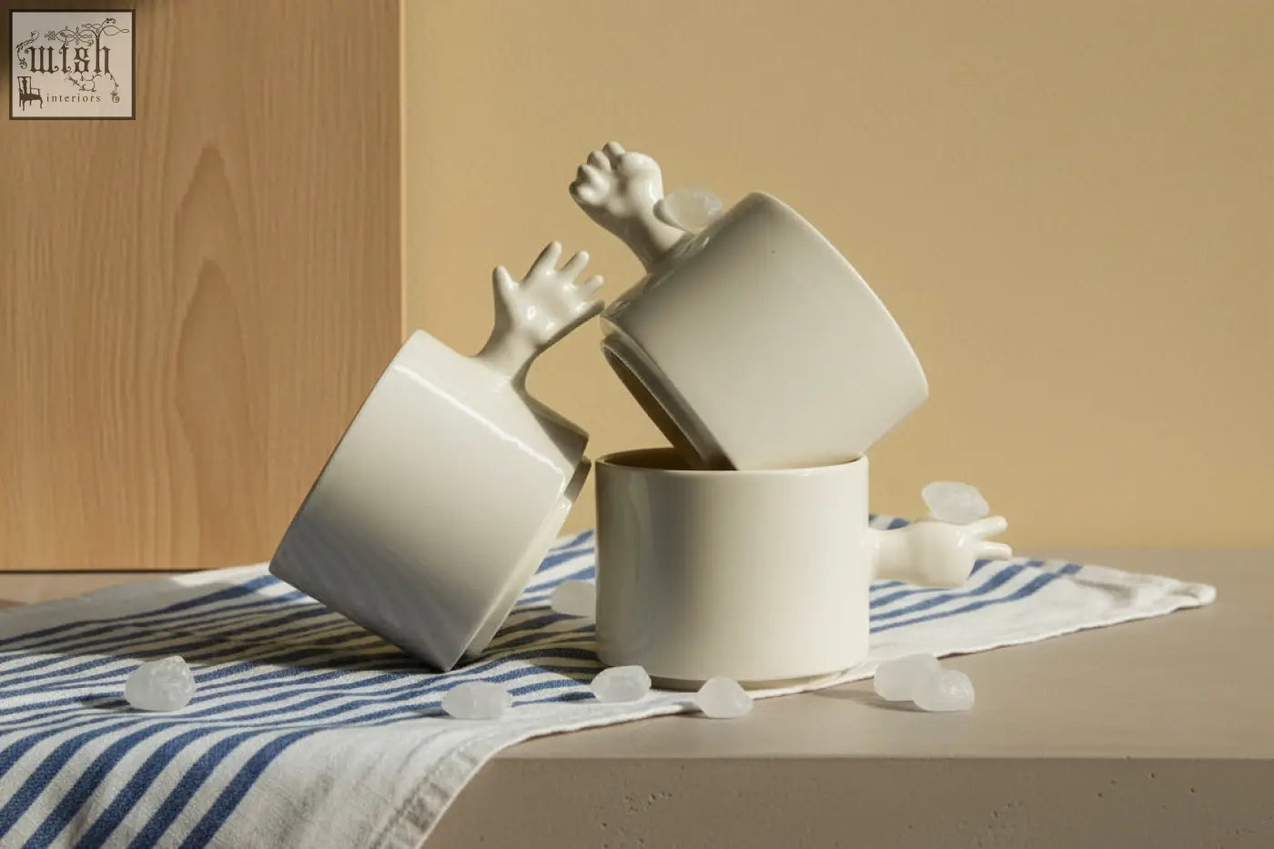 White ceramic gesture ceramic cups with sculpted hand handles stacked on striped cloth by 4am product design