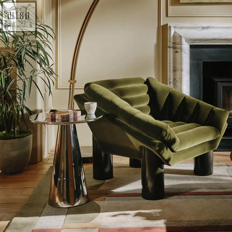 Olive green velvet armchair with sculpted cushions and black legs shown with ghosh stainless steel side table