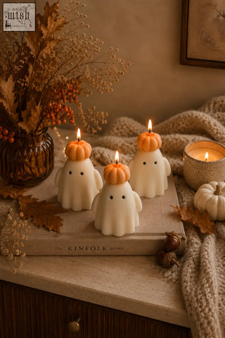 Three white ghost candles with orange pumpkin hats and lit wicks made from natural soy wax for halloween decor