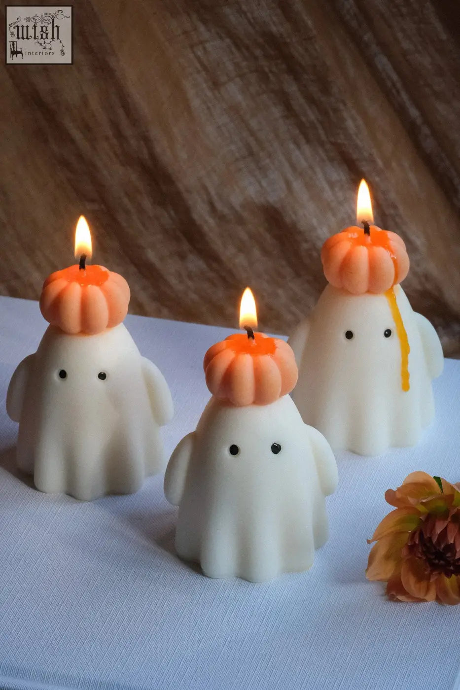 Three white ghost candles made of natural soy wax topped with orange pumpkin hats and black dot eyes