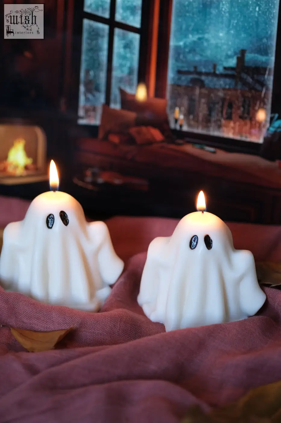 Two white ghost candles with black eyes and lit wicks perfect for spooky pumpkin spiced halloween decor