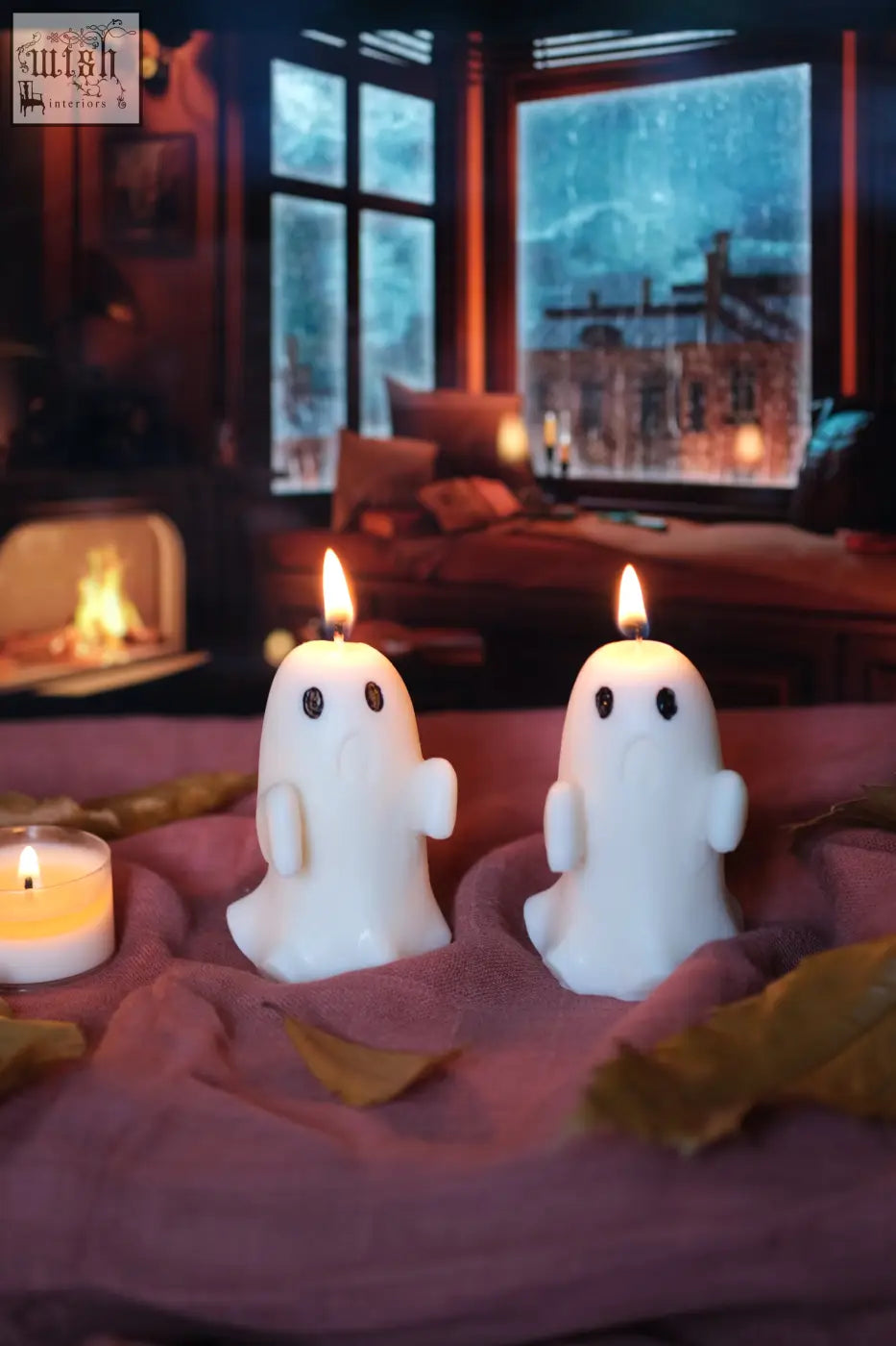 Two white ghost candles with black eyes and arms lit on pink fabric for a pumpkin spiced halloween vibe