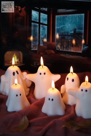 White ghost-shaped halloween candles with lit wicks on red fabric perfect for pumpkin spiced vibes and spiced latte mood
