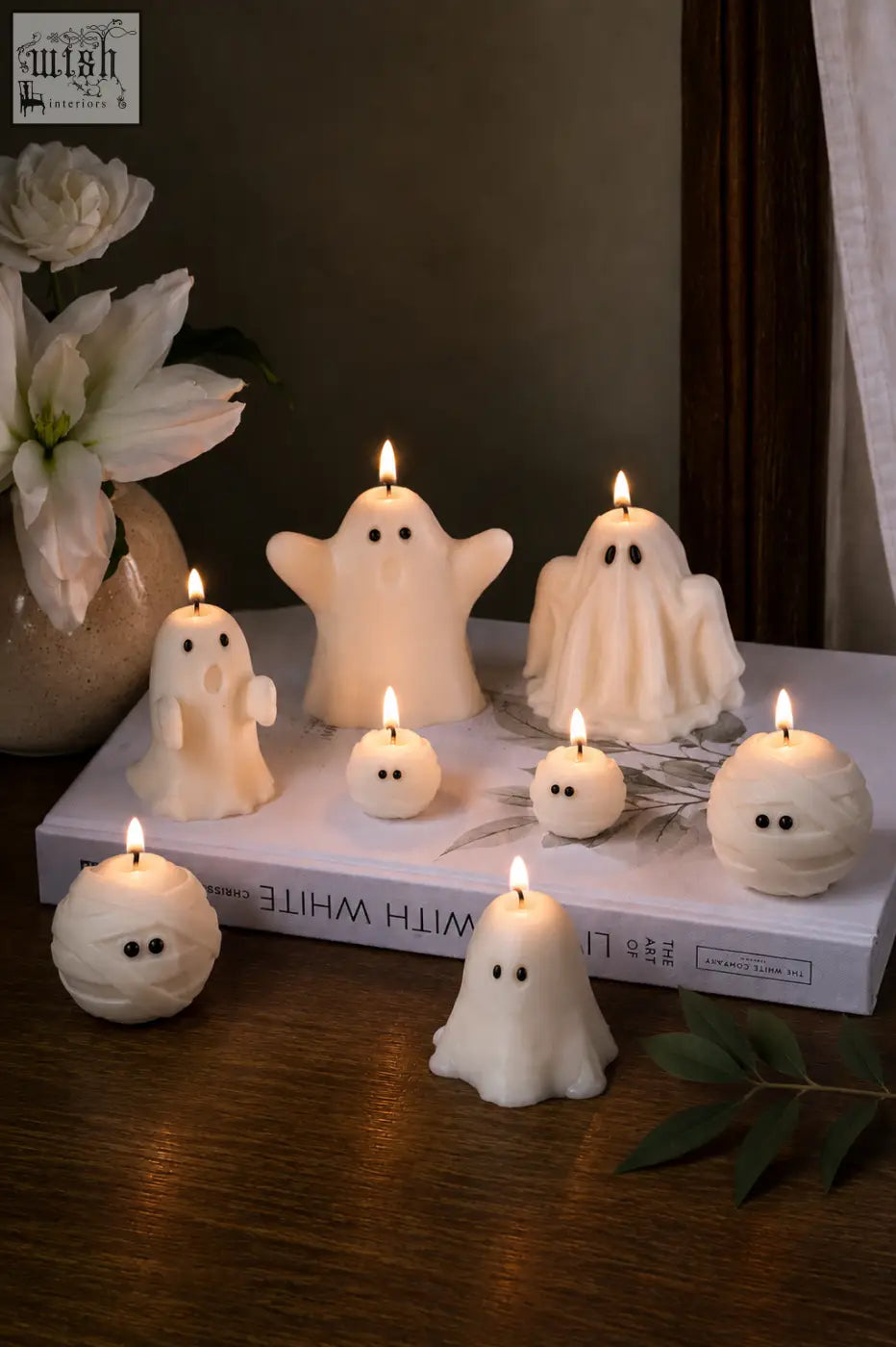 White ghost-shaped halloween candles with black eyes lit on a book perfect for a cozy pumpkin spiced vibe