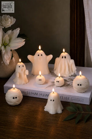 White ghost-shaped halloween candles with black eyes lit on a book perfect for a cozy pumpkin spiced vibe