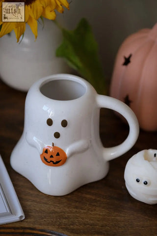 White ceramic halloween mug shaped like a ghost with black eyes holding an orange pumpkin decoration