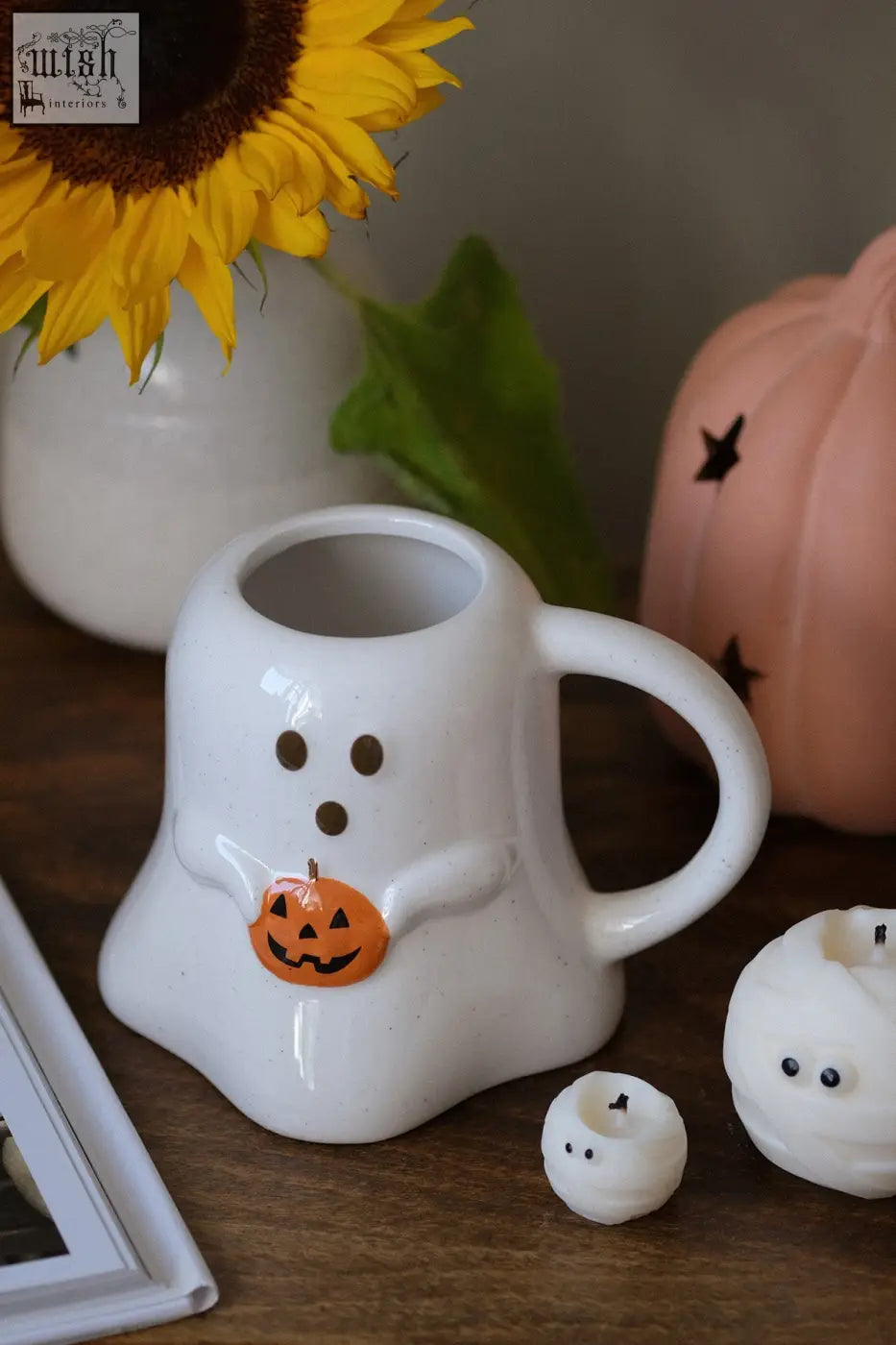 White ceramic halloween mug shaped like a ghost with black eyes and a small orange pumpkin decoration