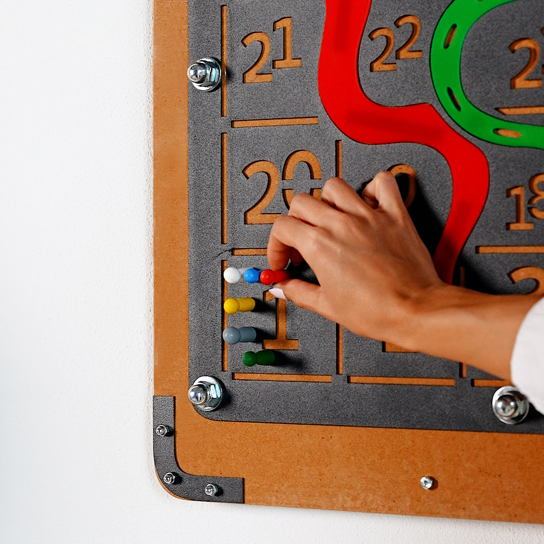 Giant snakes and ladders game board with a colorful tactile number puzzle on gray surface and brown wooden frame