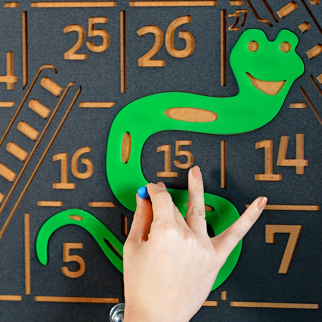 Green plastic snake with smiling face and cut-out sections from giant snakes and ladders game board