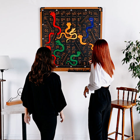 A vibrant giant snakes and ladders game board with colorful snakes and ladders on a black wood frame wall mount