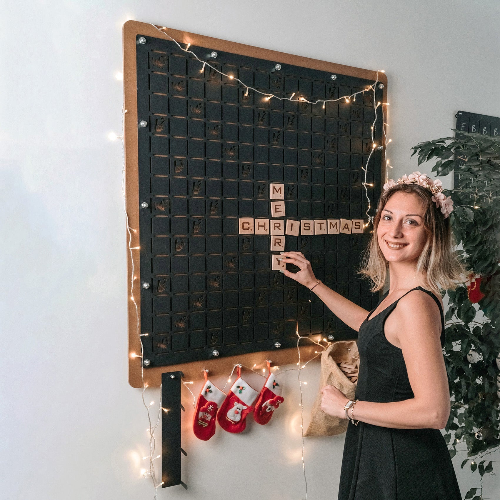 Black wooden giant words board wall game with copper frame and letter tiles spelling merry christmas and string lights