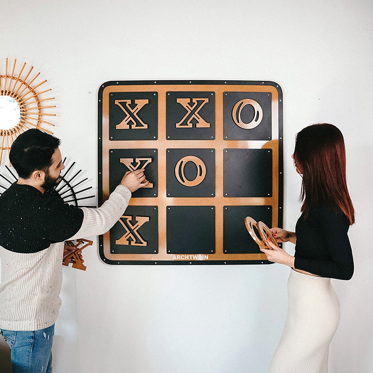 A modern wall-mounted giant xox board tic tac toe game with black surface and copper xs and os
