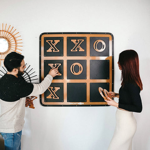 A modern wall-mounted giant xox board tic tac toe game with black surface and copper xs and os