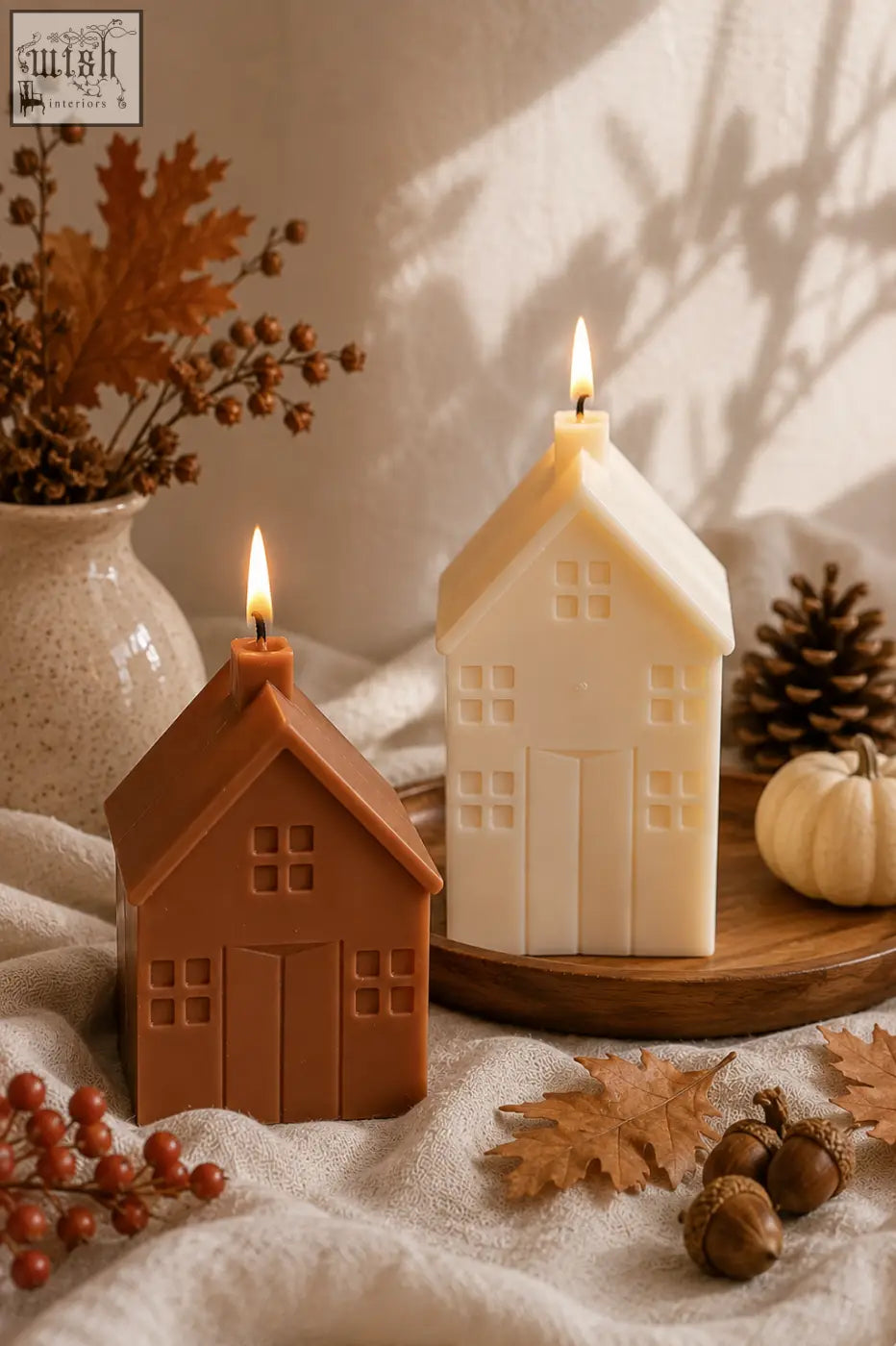 Two lit gingerbread house candles in warm terracotta and creamy off-white with detailed window and door designs