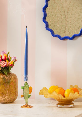 Ginny’s Glass Bass candle holder is a translucent green and orange glass fish holding a blue taper candle