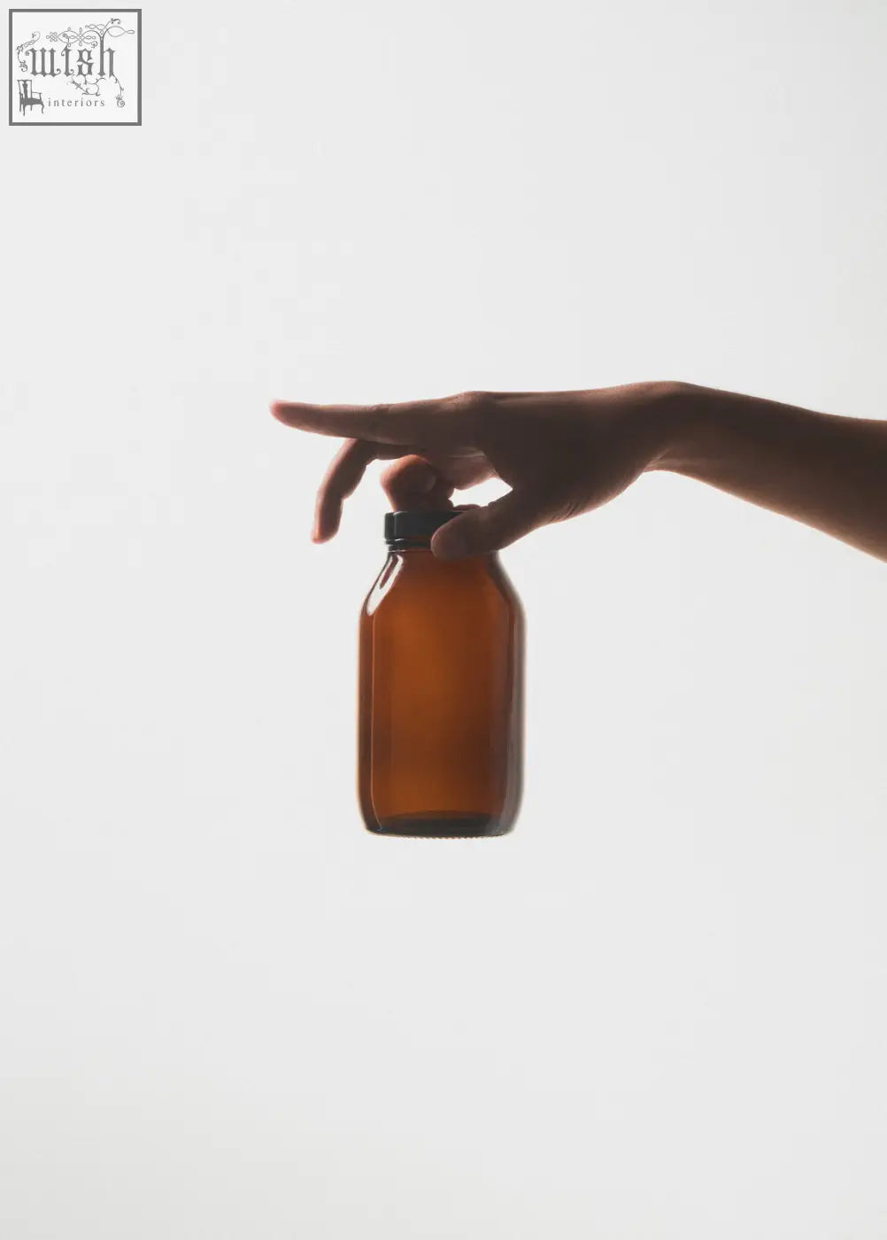 A hand holds a small amber glass storage jar with a black cap ideal for glass storage needs