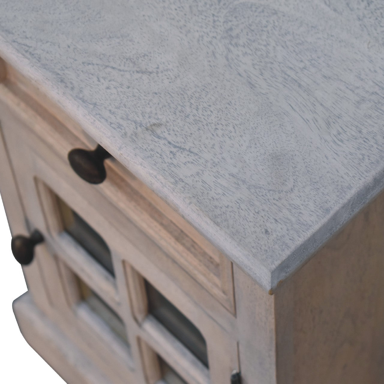 A glazed stone bedside table with a rustic light gray stone countertop and distressed wood cabinet with glass doors