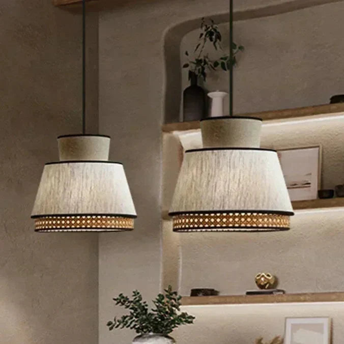 Two beige gokna light pendant lamps with tiered woven rattan and black trim hang from the ceiling
