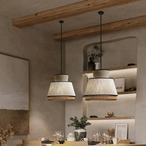 Two tiered gokna light pendant with beige textured fabric shades and gold woven accents hanging from black cords