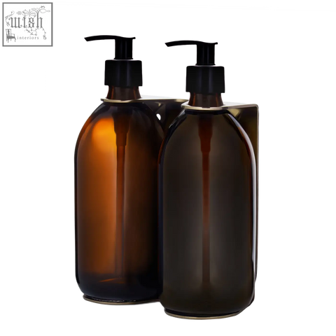 Two refillable glass bottles with black pumps in a gold double wall mounted soap dispenser with stainless steel accents