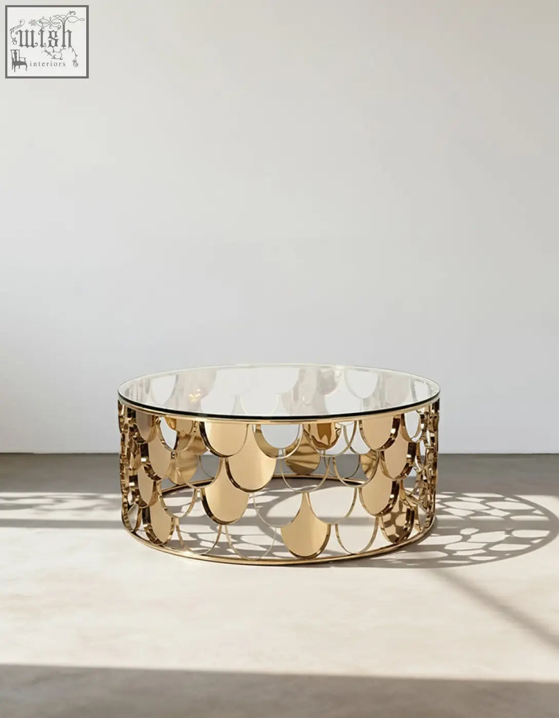 A modern gold nesting coffee table with a clear glass top and an ornate gold metal base with scale patterns