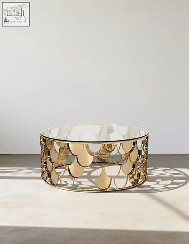 A modern gold nesting coffee table with a clear glass top and an ornate gold metal base with scale patterns