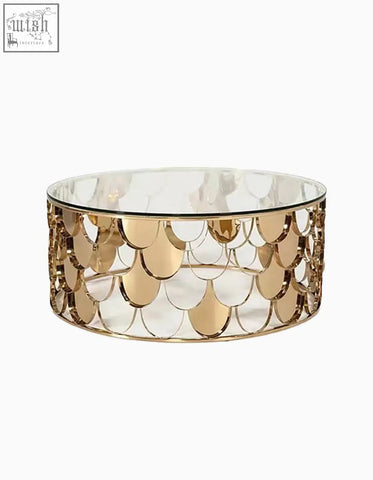 A gold nesting coffee table with a clear glass top and a gold toned metal base with a scale like pattern