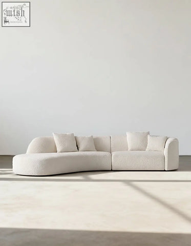 Cream-colored plush goldie gubi three seater sofa with curved boucle upholstery and matching square throw pillows