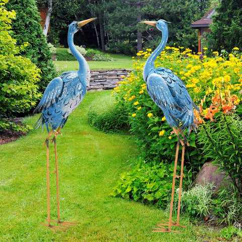 Two blue metal heron crane statues with orange beaks and legs standing on grass goodeco 96cm standing blue metal sculpture